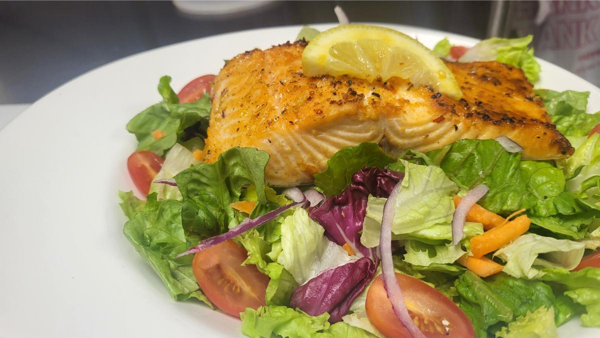 Grilled salmon salad with fresh greens, tomato, and lemon at Soul Food Factory